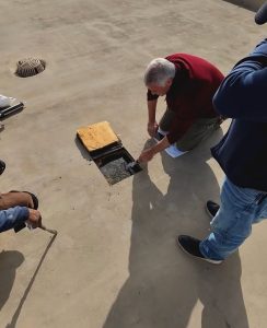 Public insurance adjusters from Rubin Adjusting performing a roof test cut during a post-fire inspection to examine roofing layers and insulation beneath the surface.
